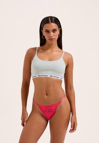 Lichtgroene bralette met zwarte logoband, gecombineerd met een felroze string met een bedrukte tekst. Zacht katoenen materiaal met dunne bandjes.