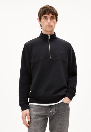 Navy half-zip pullover sweatshirt in soft fabric, featuring a structured collar, tonal logo, and ribbed cuffs and hem. Paired with gray jeans.