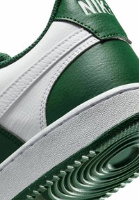 Groene en witte Nike sneaker met gestructureerd leer, gestikte details, een ronde zool met concentrische patronen en een verhoogd logo.