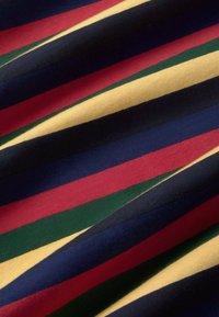 Tissu avec des rayures diagonales en rouge, jaune, vert, bleu marine et noir, montrant la texture et les plis.