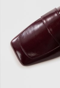 Burgundowa skórzana torebka o gładkiej, błyszczącej teksturze, prostokątnym kształcie i zamknięciu na klapę. Posiada przeszycia wzdłuż krawędzi.