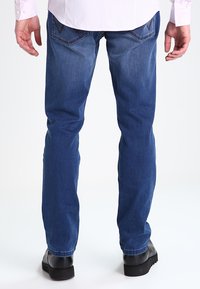 Jeans de mezclilla azul con corte recto, que presentan dos bolsillos traseros con costuras decorativas y una textura suave. Llevados con zapatos negros.