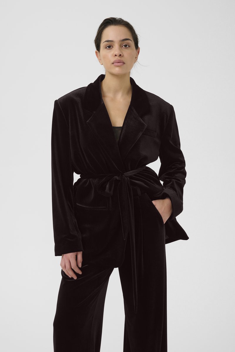 Melnas samta žaketes ar šalu, jostu viduklī un sānu kabatām. Nēsāta kopā ar atbilstošām biksēm, uzsverot gludu, greznu tekstūru.