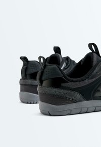 Paire de baskets athlétiques noires et grises vues de dos avec semelle texturée et languettes sur fond blanc.