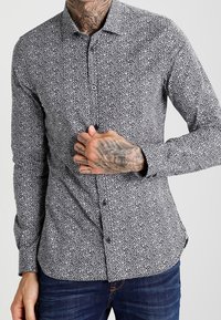 Chemise à motifs noir et blanc avec col à revers, coupe ajustée et manches longues, en tissu lisse.