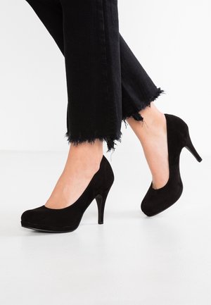 Escarpins en daim noir à bout rond et plateforme, avec un talon aiguille fin et haut. Portés avec un jean noir cropped effiloché.