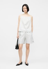 Γυναίκα με αμάνικο τοπ ανοιχτού γκρι ριγέ και σορτς μέχρι το γόνατο στον ίδιο χρωματικό τόνο, κρατώντας μαύρη τσάντα και φοράει μαύρες μπαλαρίνες.