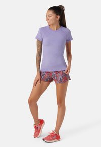 Lila träningsskjorta med korta ärmar och strukturerat mönster, kombinerad med flerfärgad blommig tryckta shorts och röda sportskor.