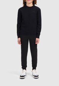 Zwarte gebreide trui met geribde ronde hals en manchetten, gecombineerd met zwarte joggers en witte sneakers met zwarte accenten. Eenvoudig, getailleerd ontwerp.