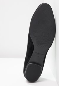 Chaussure en suède noir avec une surface lisse et une texture subtile. Dotée d'une semelle en caoutchouc avec un motif pour une meilleure adhérence. Taille 37 indiquée sur la semelle.