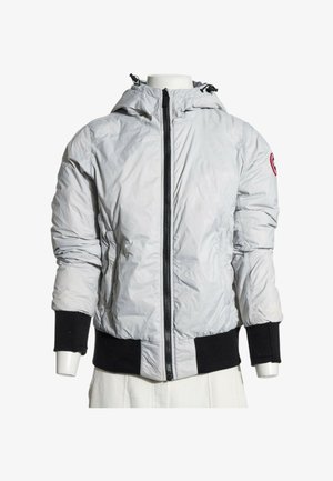 Chaqueta con capucha de color gris claro con cremallera negra, puños negros y cinturilla, exhibida en un torso de maniquí.