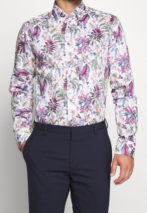 Weißes Hemd mit Knöpfen und bunten Blumen- und Blättermustern in verschiedenen Rosa-, Grün- und lilanen Tönen. Lange Ärmel, taillierte Passform, kombiniert mit dunklen Hosen.