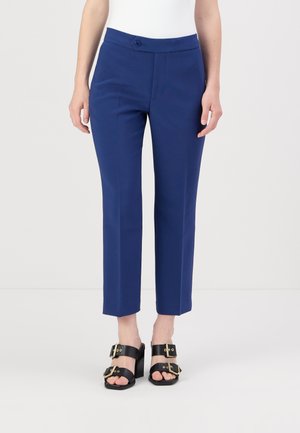 Maßgeschneiderte marineblaue Hosen mit flacher Vorderseite, Knopfverschluss und gekürztem Saum. Getragen mit schwarzen Sandalen mit Riemen und goldenen Akzenten.