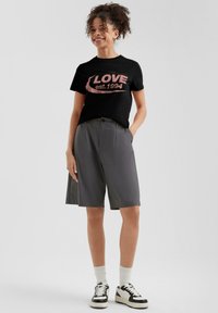 Zwarte T-shirt met roze opdruk "LOVE est. 1994", gecombineerd met grijze shorts en zwart-witte sneakers. Heeft een relaxed fit.