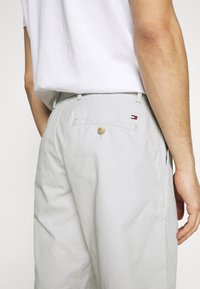 Pantalones cortos de color gris claro con un corte relajado, que cuentan con un cierre de botón en la parte posterior, bolsillos laterales y un pequeño logotipo de la marca en rojo, blanco y azul.