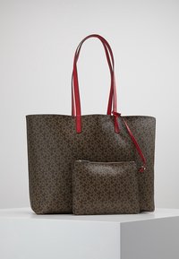 Brun tygväska med röda handtag, prydd med ett heltäckande logomönster. Inkluderar en matchande zippered väska med liknande design.