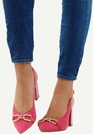 Femme portant un jean bleu et des chaussures à talons hauts rose vif avec des boucles décoratives en or et strass.