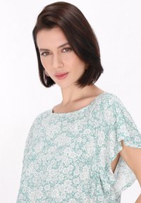 Lätt, mintgrön blus med ett blommönster i vitt, korta flytande ärmar och rund halsringning.