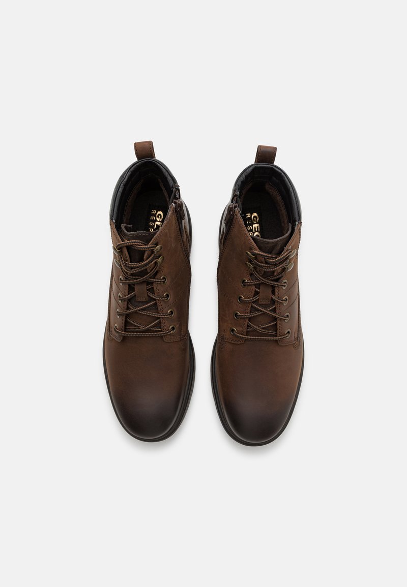 Bruine leren enkelboots met platte veters, ronde neus en treklip. Heeft een gevoerde kraag en een gestructureerde rubberen zool voor grip.