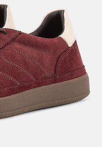 Βουργουνδίας σουέντ αθλητικά παπούτσια με κρεμ δερμάτινο τακούνι, υφασμάτινο σχεδιασμό στο πάνω μέρος και καφέ λαστιχένια σόλα. Διαθέτουν αντίθετες ραφές ως λεπτομέρειες.