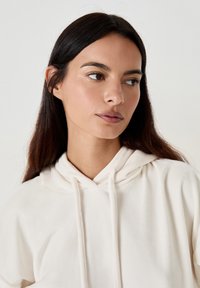 Cremfarbener Hoodie mit Kordelzug, aus weichem Stoff gefertigt. Verfügt über einen lässigen Schnitt und eine geräumige Kapuze. Minimalistisches Design ohne sichtbares Logo.