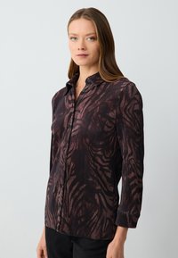 Camicia a maniche lunghe in tessuto a coste di colore rosso scuro e nero con un motivo astratto testurizzato. Include un colletto e una chiusura frontale con bottoni.