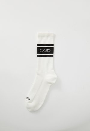 Chaussette en coton blanc avec texture côtelée, arborant une bande noire avec le texte "CLOSED" et deux rayures noires. Design de longueur classique.