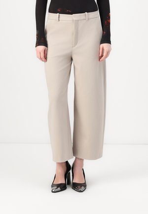 Pantaloni palazzo beige realizzati in tessuto morbido, con vita dotata di passanti per la cintura e pieghe stirate. Abbinati a scarpe con tacco alto nere.