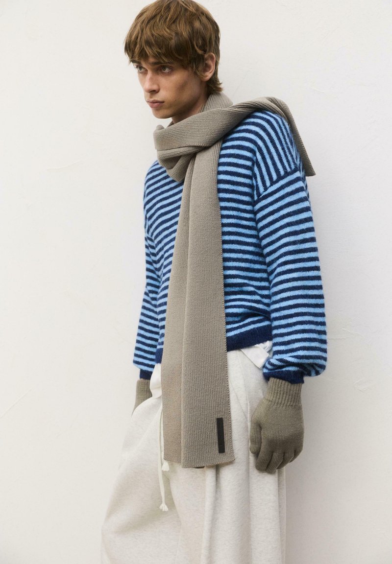Blue and navy striped sweater, beige knitted scarf, grey gloves, and light-colored pants. Soft textures and casual design.