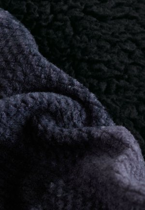 Tumedad, tekstuuriga kangakihid sügavates mereväe- ja mustades toonides, millel on pehme, fliisilaadne materjal kergete kortsudega pinnal.