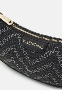 Svart dragkedjeskåp i texturerat tyg med ett upprepat vitt Valentino-logomönster och med guldtonad dragkedja som accent.