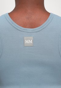 Blue ribbed tank top with a round neck and a small gray tag featuring "MM" stitched on the back. Smooth texture and fitted design.