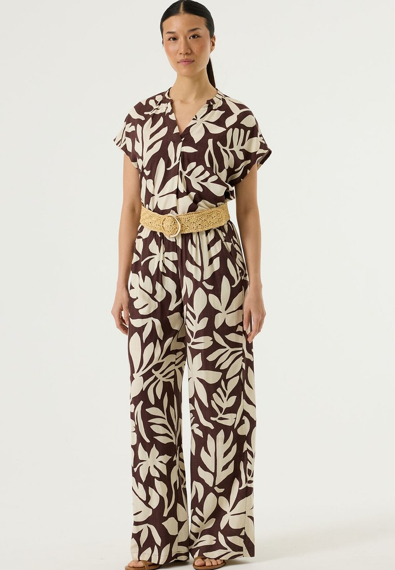 Bruin- en crèmekleurig jumpsuit met bladmotief, korte mouwen, een V-hals en wijde pijpen, getailleerd met een gele geweven riem.