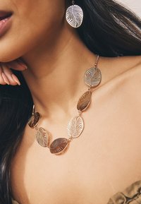 Gold-tone jewelry set featuring a necklace and matching earrings, designed with leaf motifs and intricate textures, displaying a mix of shiny and matte finishes.