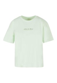 Lys grøn bomulds t-shirt med korte ærmer, rund halsudskæring, og teksten "Flutter & Bloom" trykt med en mørkere grøn skrift på forsiden.