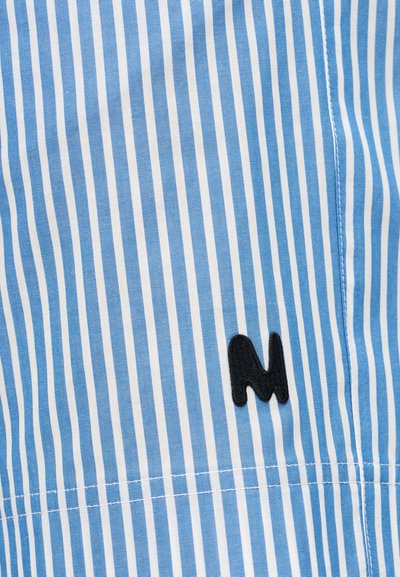 Ύφασμα με κάθετες ρίγες σε μπλε και λευκό χρώμα, με ένα μικρό μαύρο κεντητό γράμμα "Μ" κοντά σε ραφή.