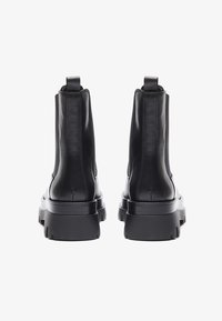 Botas de cuero negras hasta el tobillo con suela gruesa, paneles laterales elásticos y lengüetas. Textura suave con costuras mínimas y un diseño elegante.