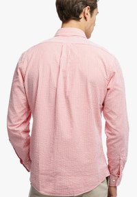 Camicia a maniche lunghe a righe rosse e bianche con colletto abbottonato, caratterizzata da uno yoke posteriore e orlo curvo, realizzata in cotone traspirante.