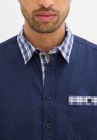 Camicia blu navy con colletto a quadretti blu e bianchi, dotata di taschino e chiusura con bottoni. Tessuto morbido, vestibilità sagomata.