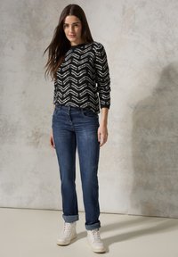 Suéter de patrón de zigzag en blanco y negro con mangas largas, combinado con jeans de mezclilla azules y zapatillas altas blancas sobre un fondo neutro.