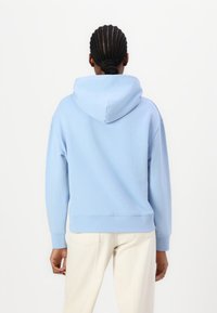 Felpa con cappuccio blu, con polsini e orlo a coste, realizzata in tessuto morbido. Presenta un design semplice e una vestibilità comoda. Indossata con pantaloni di colore chiaro.