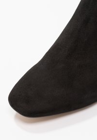 Pointe de chaussure noire en daim à bout pointu sur fond blanc avec une texture lisse et sans ornements visibles.