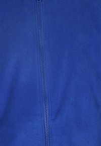 Giacca in pile blu con zip lunga e una texture morbida. Il tessuto appare liscio con un colore uniforme e senza motivi visibili.