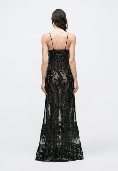 Pikkade tumedate juustega naine kannab põrandani ulatuvat läbipaistvast mustast kangast peenete mustade tikanditega kleiti, õhukeste rihmadega ning ta käte ja selja peal on nähtavad tätoveeringud.