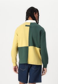 Sudadera de manga larga en diseño cuarteado de color amarillo, verde y crema. Material de mezcla de algodón con cuello y pequeño detalle de lazo en la parte posterior.