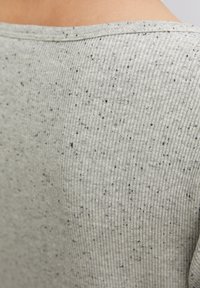 Harmaa ribbikankainen yläosa, jossa on pilkullinen tekstuuri ja pieniä mustia läiskiä sekä leveä kaula-aukko, joka esittelee pehmeää ja kevyttä materiaalia.