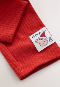 Tissu en coton rouge à texture côtelée avec une étiquette blanche affichant un cochon cartoon portant un chapeau rouge et le texte "PEPPA PIG".