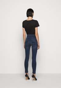 Jeans de mezclilla oscuros de tiro alto con un diseño ajustado, que cuentan con bolsillos traseros y detalles de costura sutiles, llevados con una camiseta negra y tacones.