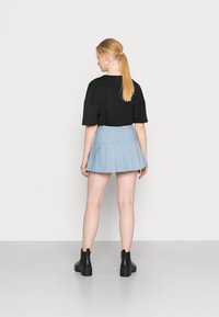 T-shirt oversized preto, saia mini pregueada azul clara com riscas verticais e botas de tornozelo pretas. Textura suave, design casual.