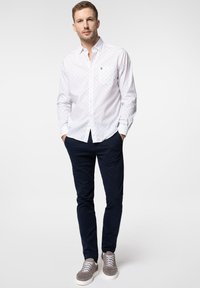 Biała koszula z guzikami i małymi niebieskimi kropkami, kieszonką na piersi, w połączeniu z ciemnogranatowymi spodniami oraz szarymi trampkami. Gładka faktura i casualowy design.